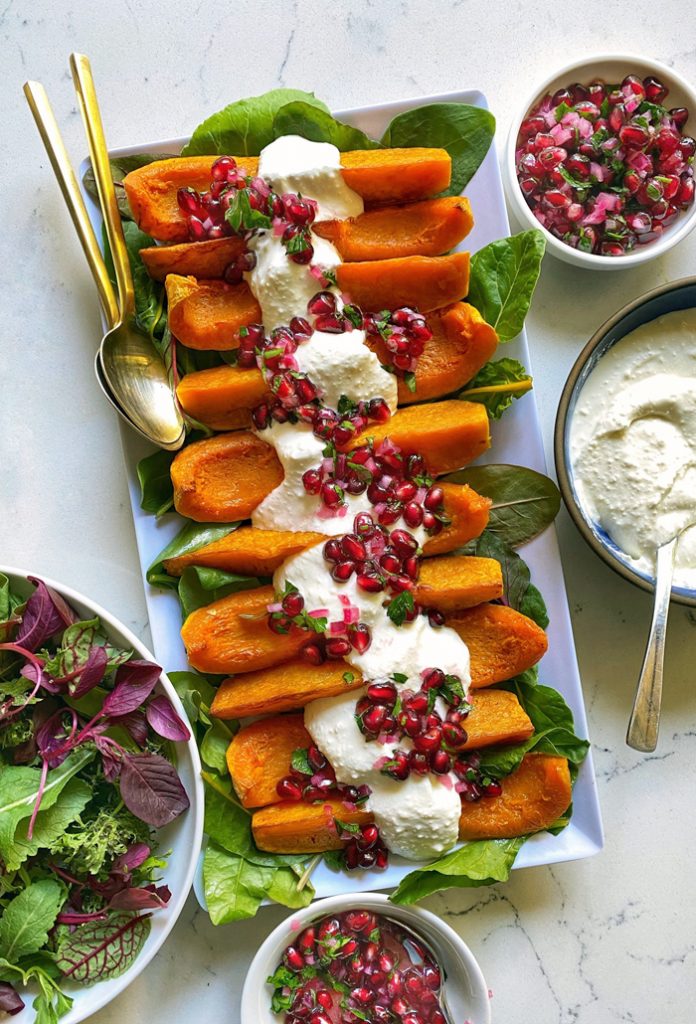 roasted butternut squash wedges with whipped feta and pomegranate salsa on top on rectangular plate 